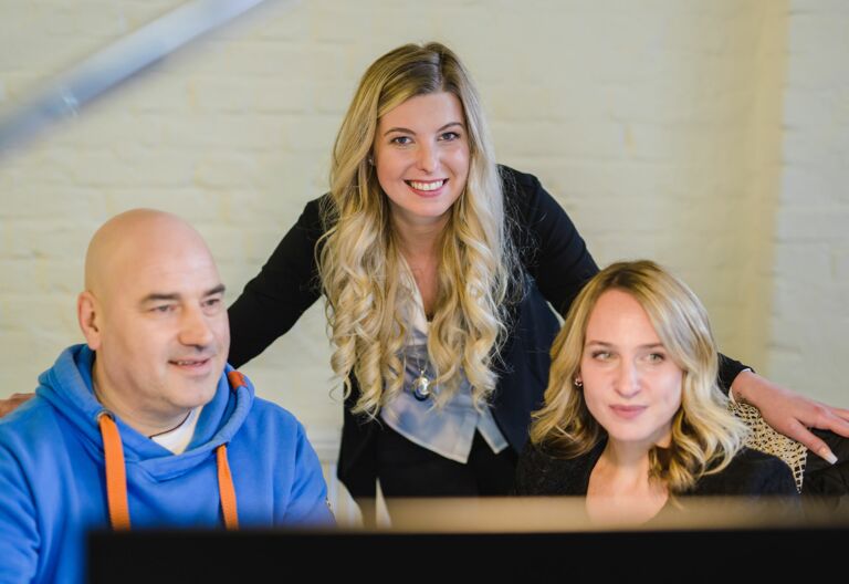 NOVIA GmbH Consulting und Baumanagement - Momentaufnahme Gespräch von Kollegen am Platz. Kollegin schaut über die Schulter und freundlich in die Kamera.