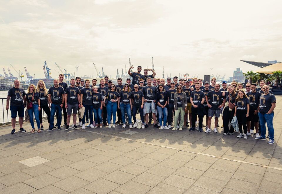 NOVIA GmbH Consulting und Baumanagement - Gruppenbild des gesamten Teams beim Sommerfest 2023. Hamburger Hafen im Hintergrund.