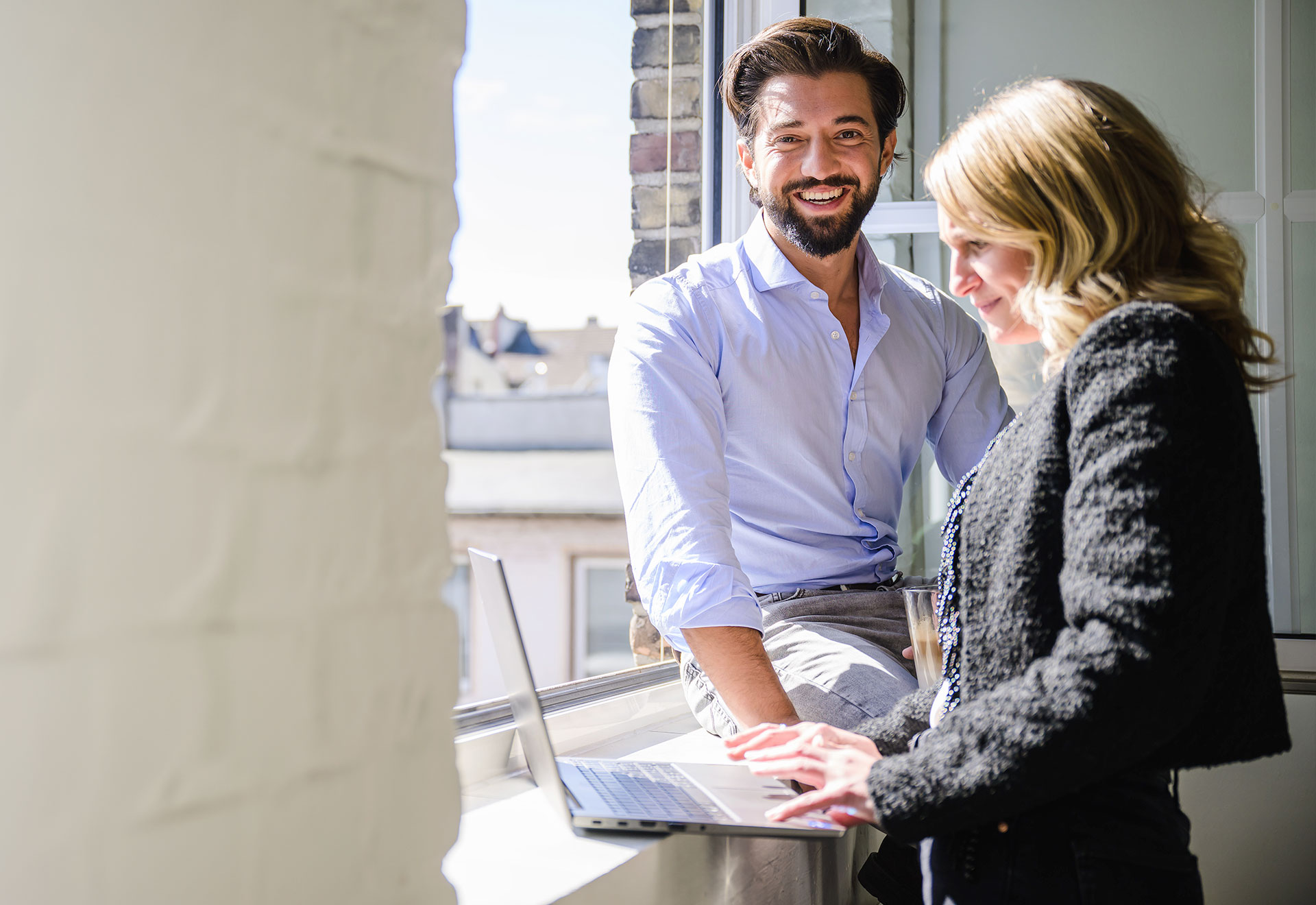 NOVIA GmbH Consulting und Baumanagement - Junge Kollegen besprechen sich in lockerer Atmosphäre am Fenster in der Sonne